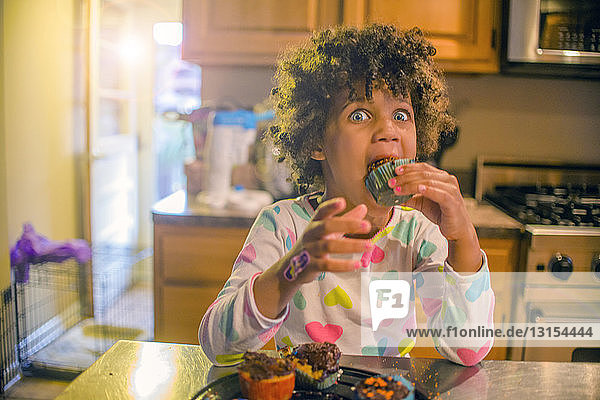 Porträt eines überraschten Mädchens  das an der Küchentheke Muffins isst