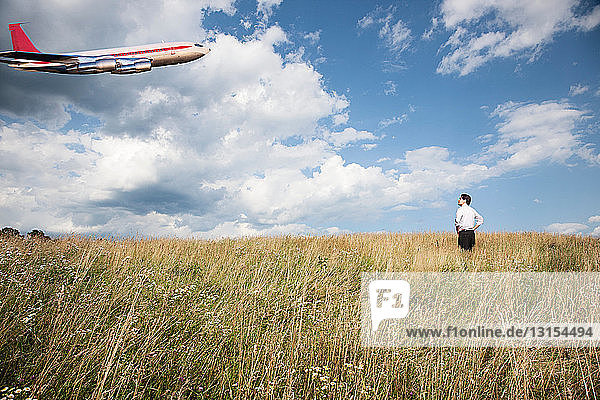 Geschäftsmann im Feld mit Blick auf ein Flugzeug