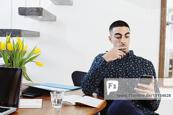 Young man sitting at table using smartphone
