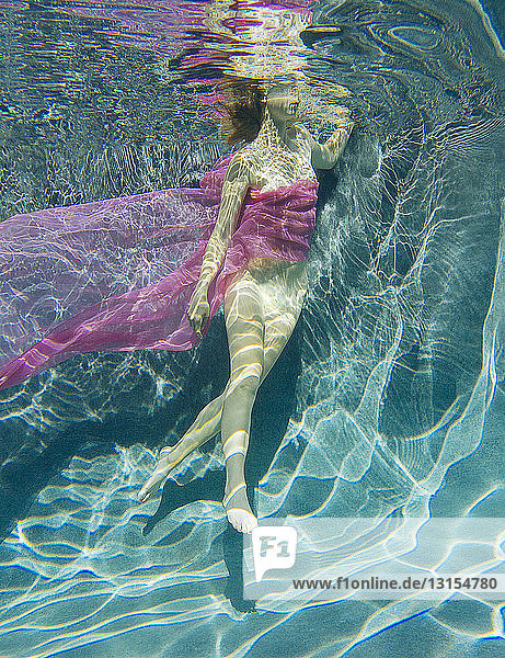 In Stoff gehüllte Frau schwimmt halbnackt unter Wasser