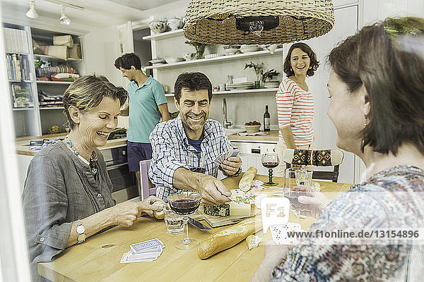 Five adult friends playing cards at dining table
