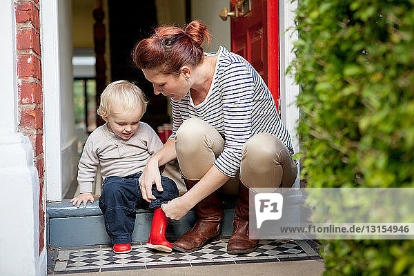 Mutter hilft ihrem kleinen Sohn beim Anziehen der Gummistiefel