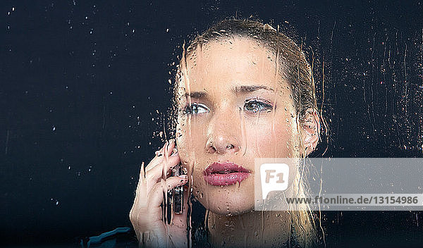 Frau am regnerischen Fenster mit Telefon