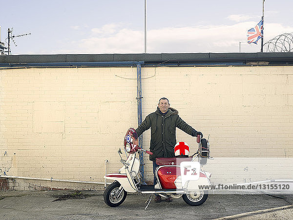 Porträt eines reifen männlichen Mods mit Moped vor einer Wand