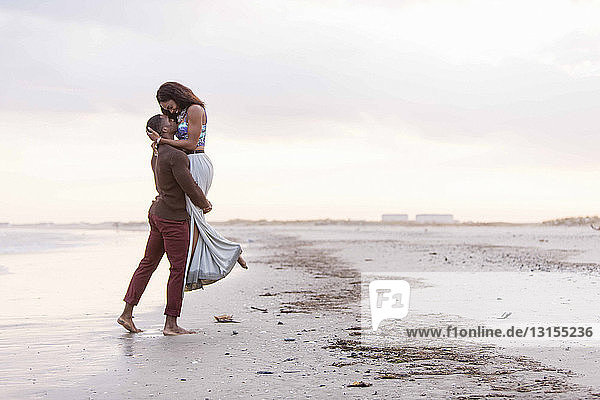 Paar am Strand  Umarmung  von Angesicht zu Angesicht  Mann hebt Frau hoch