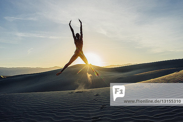 Nackte Frau in der Wüste mit erhobenen Armen in der Luft springend