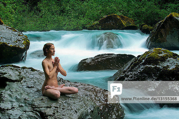 Nackte Frau meditiert auf einem Felsen am Wasser