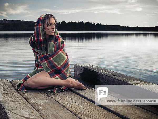 Woman in blanket on dock by lake