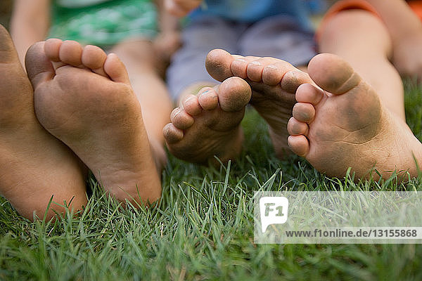 Drei Kinder sitzen mit schmutzigen Füßen im Gras