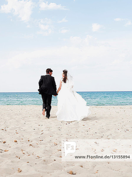 Braut und Bräutigam laufen am Strand entlang
