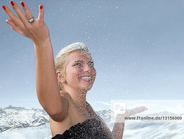 Junge Frau mit erhobenen Händen im fallenden Schnee
