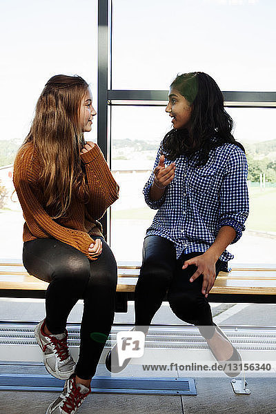 Zwei Teenager-Schülerinnen sitzen plaudernd im Korridor