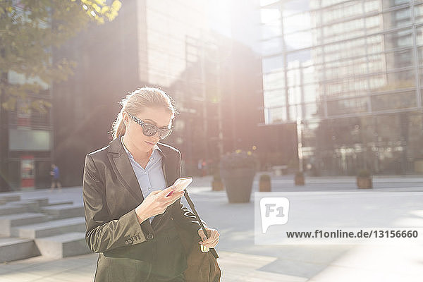 Young businesswoman outside city office reading smartphone texts