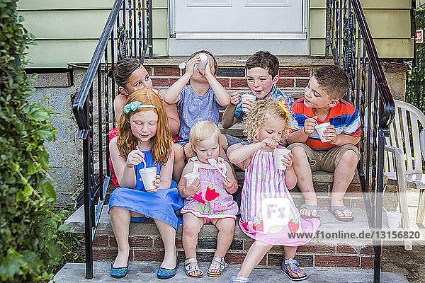 Sieben Kinder sitzen vor der Tür und essen Eis