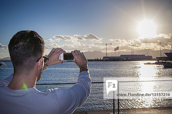 Young man taking photograph of sunset by port  Cagliari  Sardinia  Italy