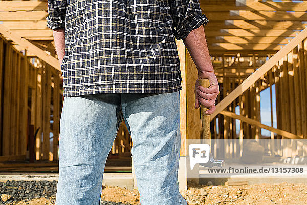 Mann mit Hammer vor dem Rahmen eines neuen Hauses