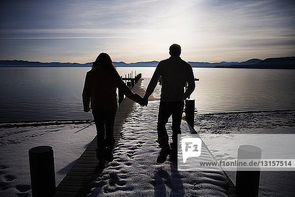 Paar spaziert auf verschneiter Seebrücke bei Sonnenuntergang