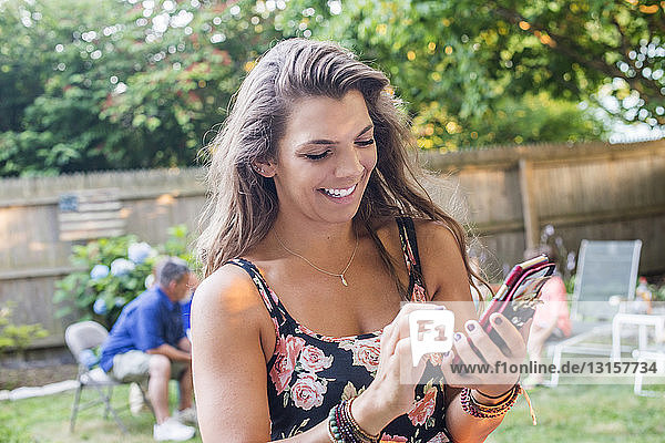 Frau  die auf einer Party im Garten eine SMS auf ihrem Smartphone schreibt
