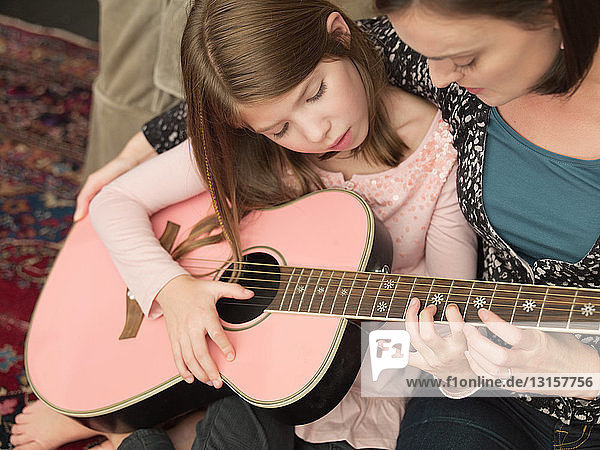Mittlere erwachsene Frau bringt ihrer Tochter das Gitarrenspiel bei