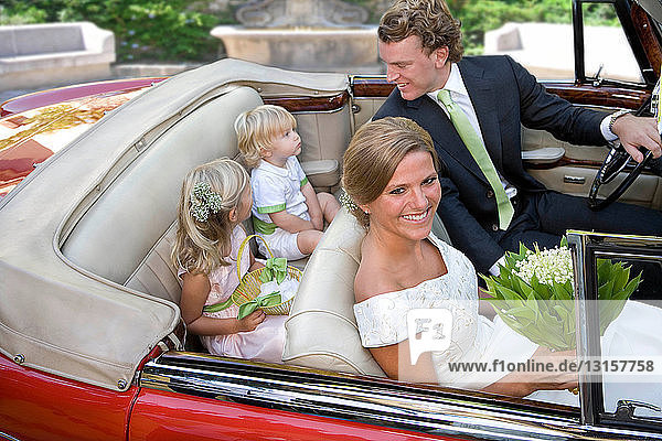 Hochzeitspaar mit Kindern im Auto
