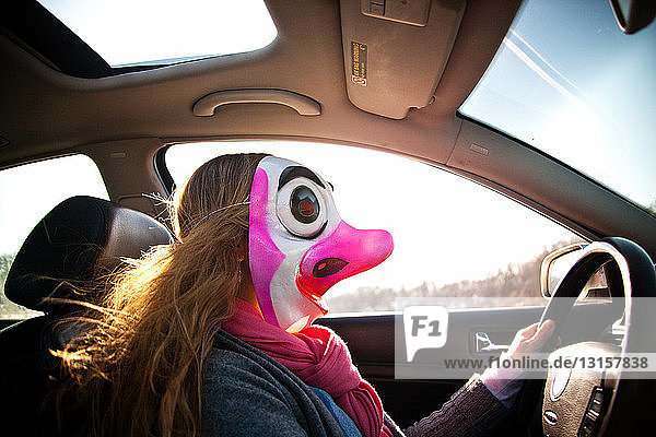 Frau fährt Auto mit Clownsmaske