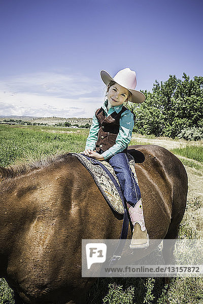 Mädchen mit Cowboystiefeln und Hut auf einem Pferd