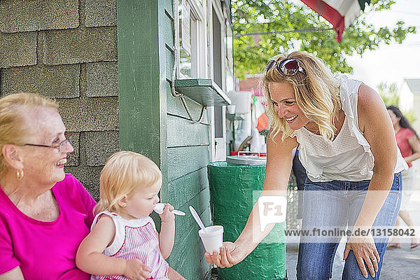 Eisverkäuferin reicht einem kleinen Mädchen und seiner Großmutter ein Eis