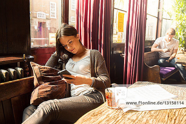 Mittlere erwachsene Frau sitzt und schaut auf ihr Smartphone