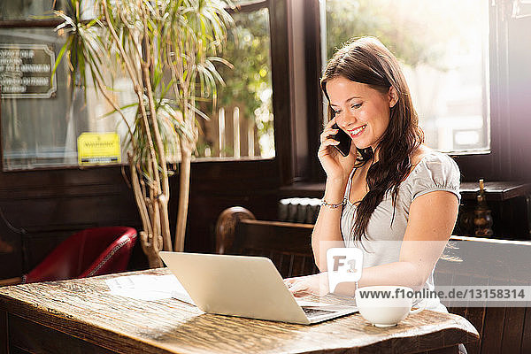 Mid adult woman sitting using laptop and smartphone smiling