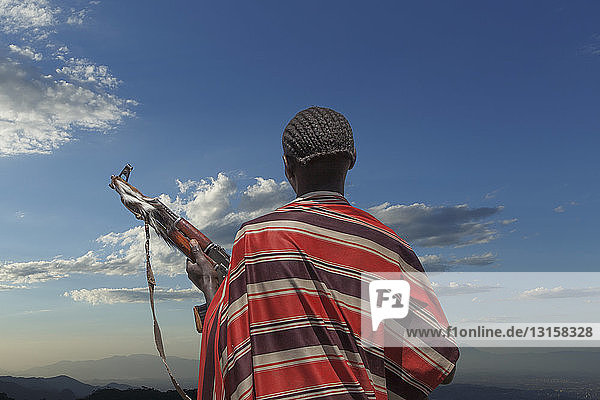 Rear view of young man from Karo tribe with Kalashnikov rifle  watching his herd   Ethiopia  Africa