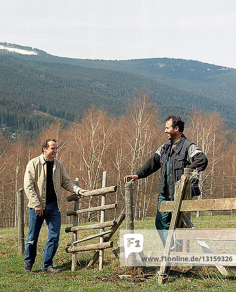Two men talking over fence and gate