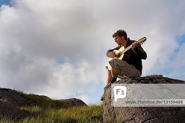Junger Mann spielt Gitarre in einer Landschaft