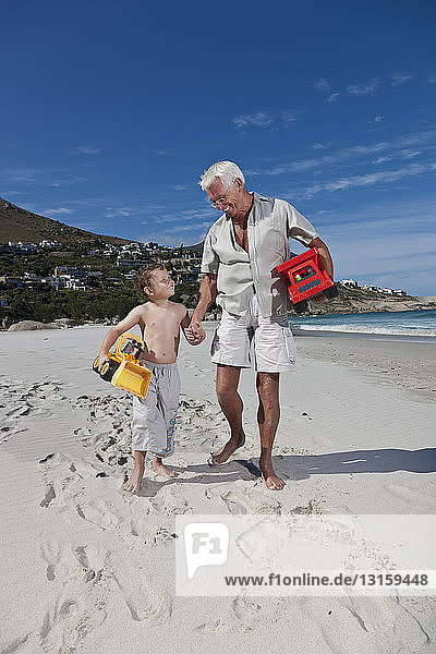 Mann hält die Hand seines Enkels am Strand