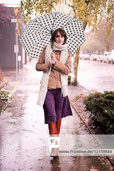 Frau geht im Regen unter Regenschirm