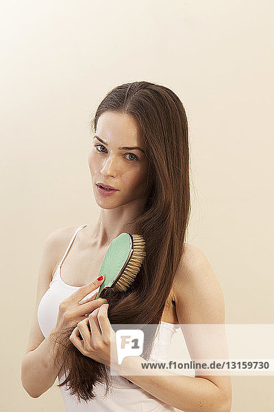 Porträt einer jungen Frau  die sich die Haare bürstet und in die Kamera schaut