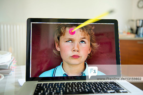 Boy looking up from laptop screen at toy arrow