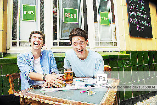 Smiling men drinking beers at cafe
