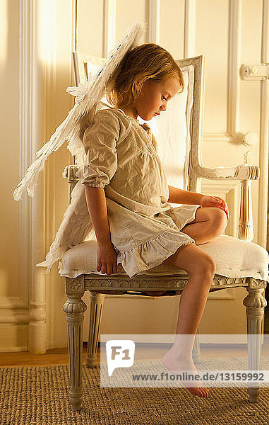 Kleines Mädchen auf Stuhl als Engel verkleidet