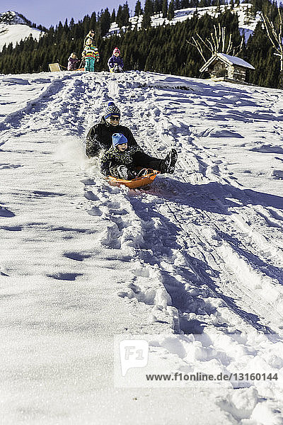Father and son riding sled down snow-covered slope  Achenkirch  Tirol  Austria