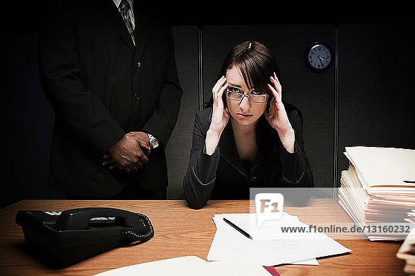 Chef hinter gestresster Frau am Schreibtisch