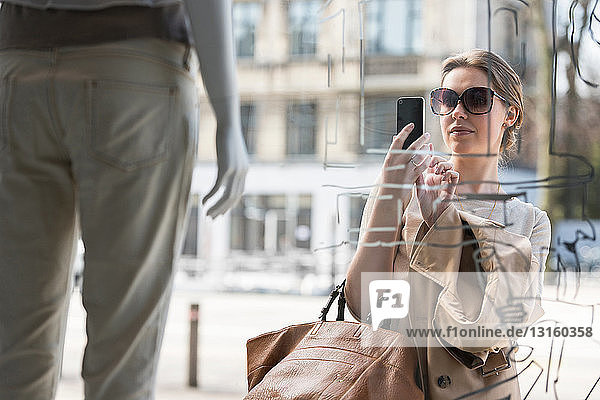 Junge Frau fotografiert Mode Schaufensterpuppe außerhalb Modegeschäft