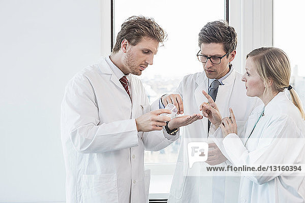 Drei Personen in Laborkitteln stehen und betrachten den Inhalt eines Reagenzglases