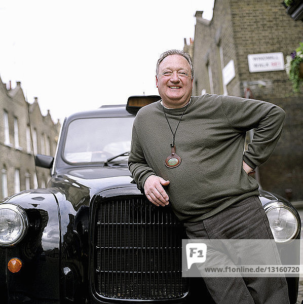 Porträt eines Taxifahrers  der sich an ein schwarzes Taxi lehnt  London  UK