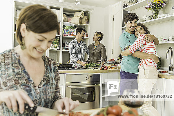 Five adult friends preparing food and chatting in kitchen