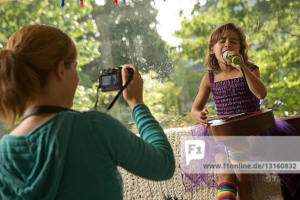 Mother photographing daughter singing with microphone