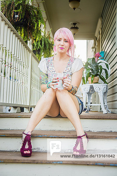 Porträt einer jungen Frau mit rosa Haaren  die auf einer Veranda sitzt