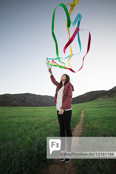 Young woman standing in field holding up dance ribbons