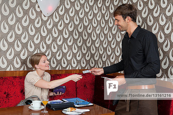Woman paying waiter with card in cafe