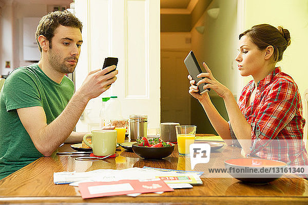 Man using smartphone and woman using digital tablet at breakfast