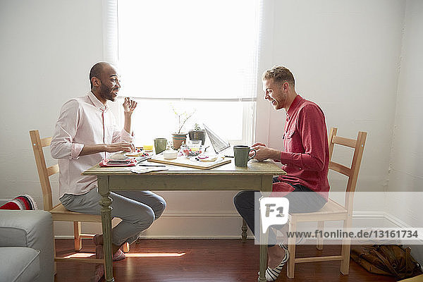 Seitenansicht von Männern  die am Esstisch sitzen und lachend frühstücken